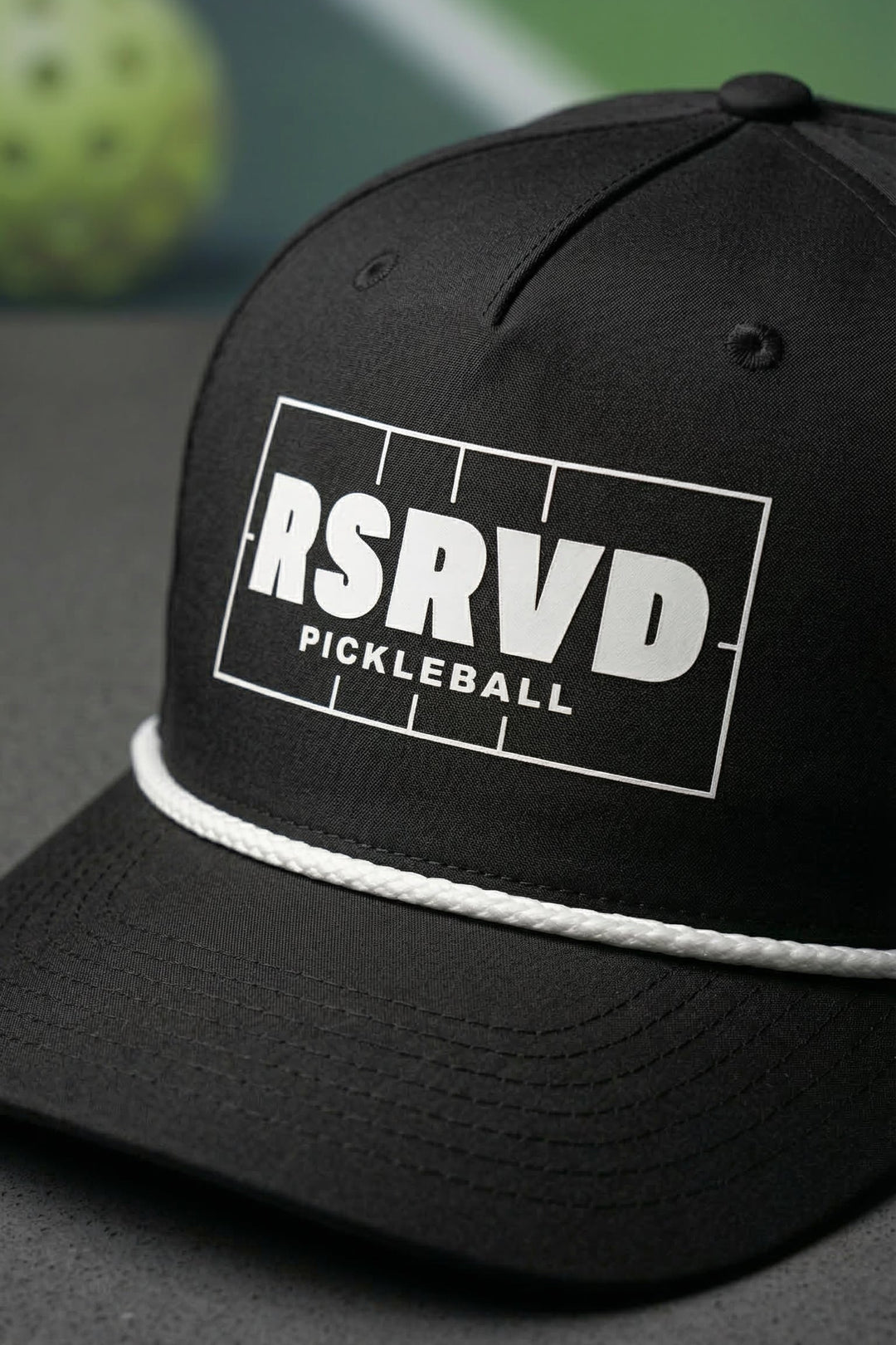 Black cap with 'RSRVD Pickleball' logo on a pickleball court background