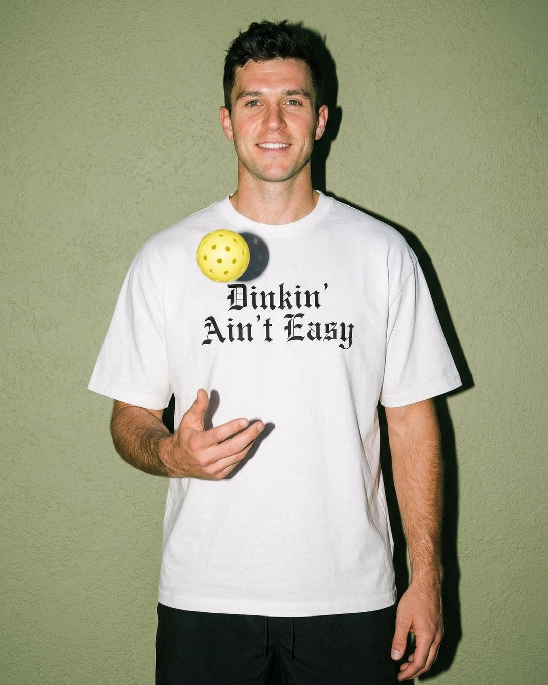 Person wearing a white t-shirt with a graphic and text against a green wall