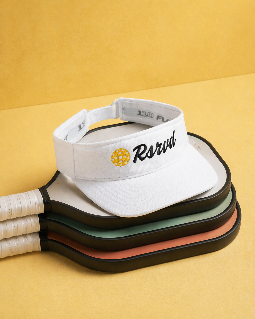 Stack of white visors with 'Rsrvd' logo on a yellow background