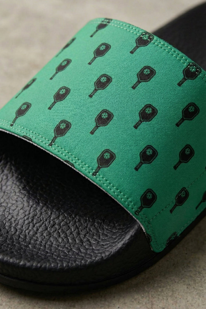 Black slide sandal with green strap featuring black pattern on a neutral background