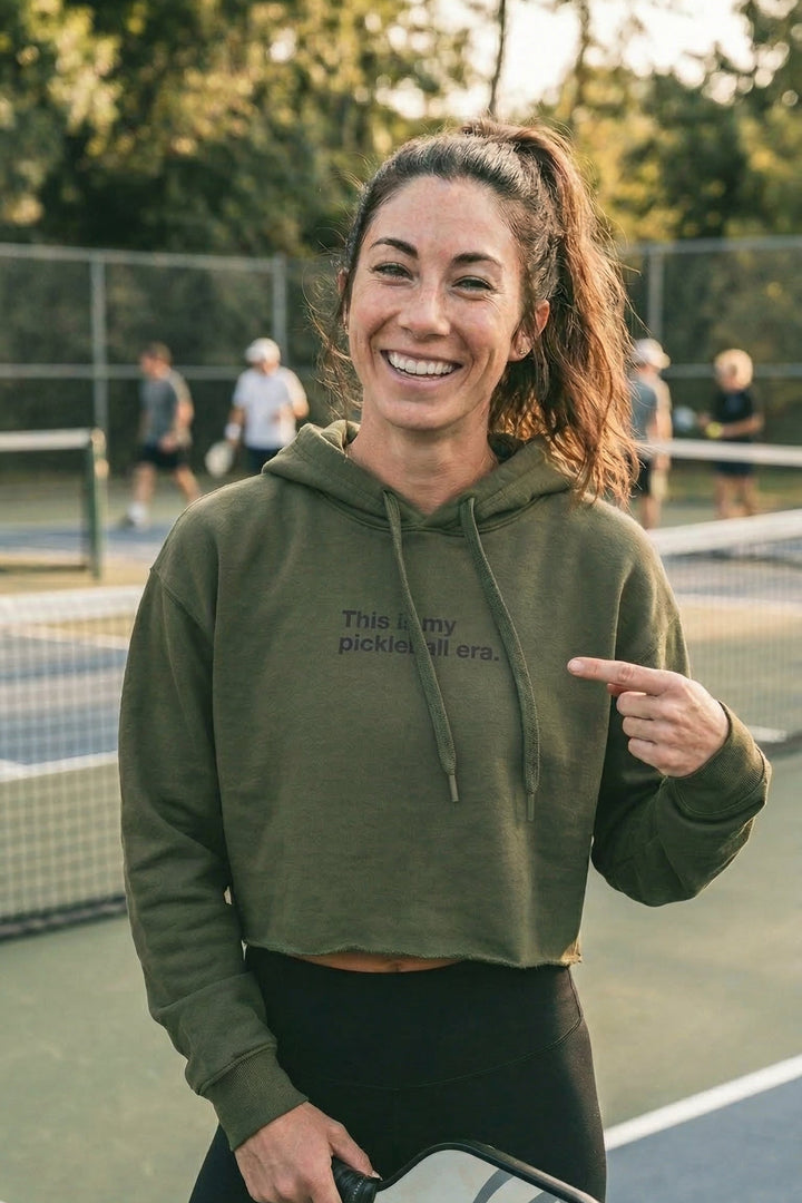 Woman in green hoodie on a pickleball court pointing at text